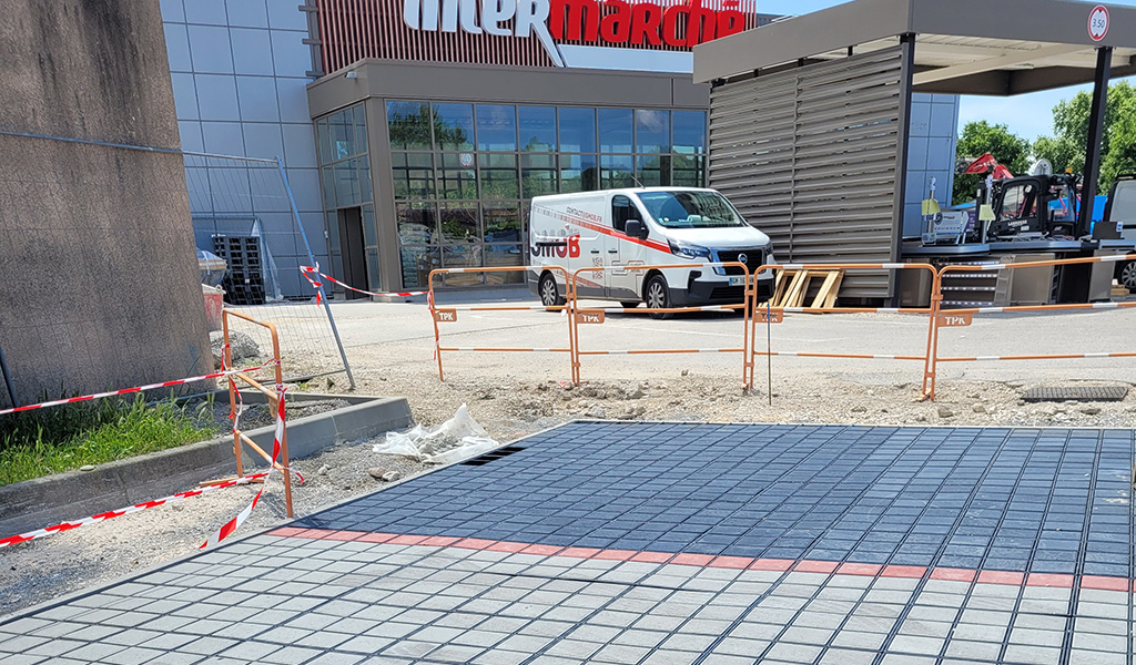 Pose de dalles drainantes alvéolaires sur parking de supermarché en cours de chantier — solution perméable Ocity PAV65 Nidaplast